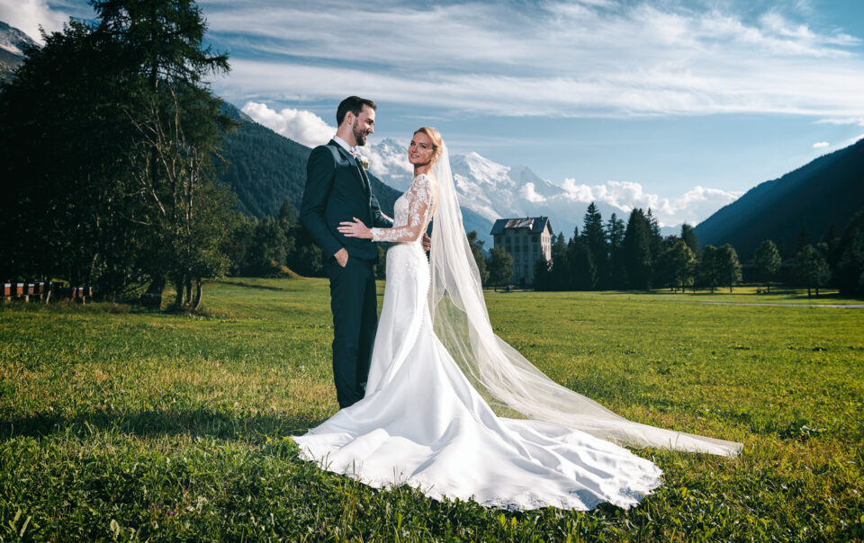 Mariés posant dans un champ avec vue sur le Mont Blanc – Photographe mariage Chamonix Haute-Savoie